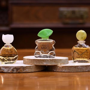K&ouml;nnte beinhalten: Drei Miniatur-Parf&uuml;mflaschen mit dekorativen Verschl&uuml;ssen werden auf Holzscheiben pr&auml;sentiert. Die Flaschen sind klar, mit einer goldenen Fl&uuml;ssigkeit gef&uuml;llt und mit Etiketten versehen. Die Verschl&uuml;sse sind wei&szlig;, gr&uuml;n und gelb. Die Flaschen sind auf einer Holzoberfl&auml;che angeordnet.