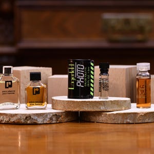 K&ouml;nnte beinhalten: Eine Auswahl an Parf&uuml;mflaschen und -fl&auml;schchen, darunter die Marken Paco Rabanne und Lagerfeld. Die Flaschen werden auf Holzplattformen und -bl&ouml;cken pr&auml;sentiert, wobei die Lagerfeld-Flasche mit "PHOTO" beschriftet ist. Die D&uuml;fte sind in verschiedenen Gr&ouml;&szlig;en und Farben erh&auml;ltlich.