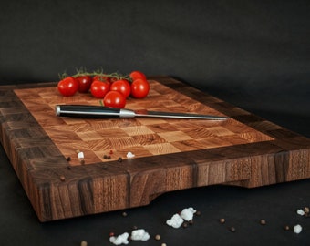 May include: A large wooden cutting board with a checkered pattern made from walnut and oak wood. A black knife and red tomatoes are on the board.