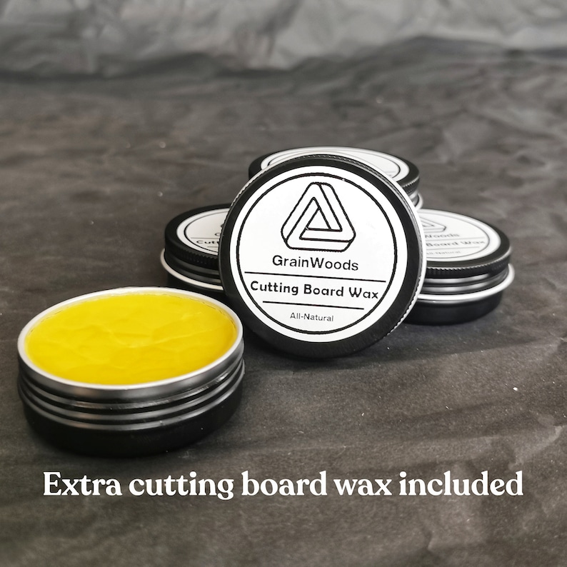Puede incluir: Un primer plano de un peque&ntilde;o tarro de cera para tabla de cortar totalmente natural. El tarro es negro con una etiqueta blanca que dice "GrainWoods Cutting Board Wax All-Natural". Hay varios tarros de cera en la imagen.