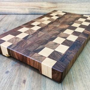 May include: A large, rectangular chopping board made of walnut and maple wood. The board has a checkerboard pattern and is engraved with the text "The Smiths Kitchen".