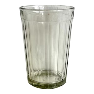 May include: A clear glass drinking glass with a ribbed design. The glass is tall and cylindrical with a rounded bottom.