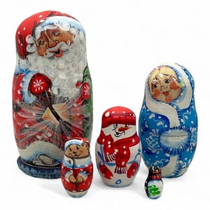Pode incluir: Um conjunto de seis bonecas russas, ou matrioskas, com desenhos festivos de férias de inverno. A boneca maior retrata o Papai Noel, enquanto outras mostram um boneco de neve, uma menina com casaco de inverno, um urso e um pinguim. As bonecas são pintadas em vermelho, azul e branco.