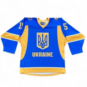 Peut inclure: Un maillot de hockey bleu et jaune avec les armoiries ukrainiennes et le mot "UKRAINE" sur le devant.