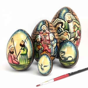 May include: Set of six wooden eggs decorated with scenes from the Nativity story. The eggs are painted in vibrant colors and feature details like a star, a shepherd, and a lamb.