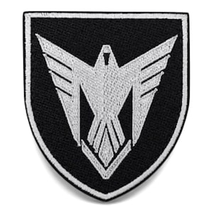 Peut inclure: Écusson brodé noir et blanc en forme de bouclier. Le patch présente un motif d'oiseau stylisé blanc sur fond noir. L'oiseau a des ailes déployées et un design géométrique. Le patch a une bordure blanche.