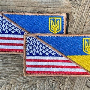 May include: Two embroidered patches featuring a combined design of the American and Ukrainian flags. The American flag portion has red and white stripes with white stars on a blue field. The Ukrainian flag has a blue and yellow design with a yellow trident.