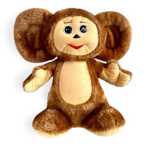 May include: A brown plush toy monkey with large ears, black eyes, and a red mouth. The toy is sitting on a white background.