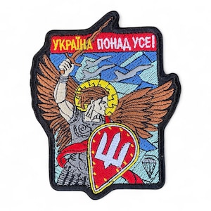 Könnte beinhalten: Gestickter Aufnäher mit einem Engel mit Schwert und Schild, mit dem Text "UKRAINE ÜBER ALLEM!" in Rot. Der Aufnäher hat einen schwarzen Rand und einen blau-weißen Hintergrund.