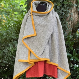 May include: A gray and white herringbone patterned cloak with a mustard yellow trim and a matching hood. The cloak is fastened with a decorative clasp and is displayed over a red garment.