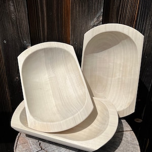 Könnte beinhalten: Eine Sammlung unfertiger Holzschalen in verschiedenen Größen und Formen. Die Schalen sind hell, mit glatten Oberflächen und abgerundeten Kanten. Sie sind auf einem Holzstumpf und vor einem dunklen Holzhintergrund angeordnet.