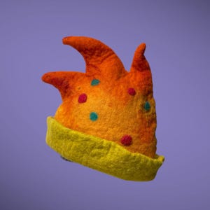 Może przedstawiać: Kapryśny, ręcznie robiony kapelusz filcowy w odcieniach pomarańczu i żółci. Kapelusz ma kształt korony z trzema punktami i jest ozdobiony kolorowymi kropkami. Rondo jest w kolorze jasnożółtym, tworząc zabawną i unikalną ozdobę.