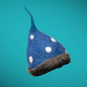 Może przedstawiać: Niebieski filcowy kapelusz z białymi kropkami i brązowym rondem. Kapelusz ma spiczasty wierzch. Kapelusz jest ustawiony na turkusowym tle. Ten fantazyjny kapelusz nadaje się do kostiumów lub na co dzień.