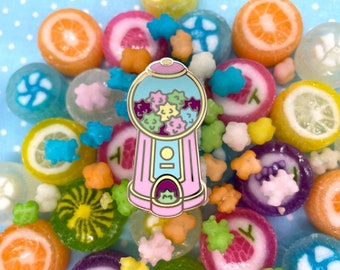 May include: A pink and blue gumball machine pin with a clear window showing colorful star-shaped gumballs. The pin is surrounded by a variety of colorful candy, including lemon drops, hard candies, and gumdrops.