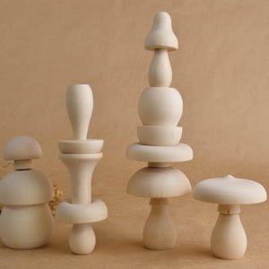May include: Four unfinished wooden mushroom-shaped toys of varying sizes. The toys are light in color and have a smooth, natural finish. The mushrooms have different designs, some with stacked elements, and are arranged on a neutral background.