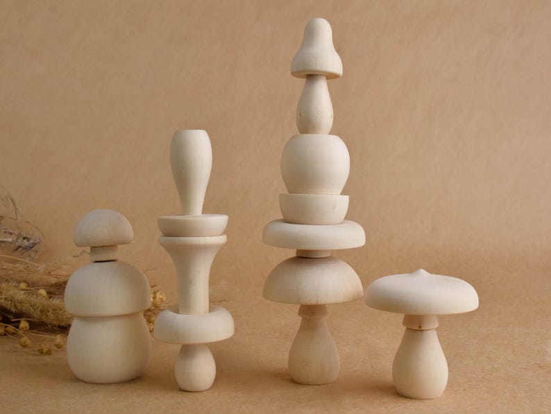 May include: Four unfinished wooden mushroom-shaped toys of varying sizes. The toys are light in color and have a smooth, natural finish. The mushrooms have different designs, some with stacked elements, and are arranged on a neutral background.