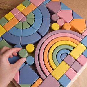 May include: A set of colorful wooden blocks in various shapes and sizes, including circles, squares, rectangles, and arches. The blocks are arranged in a pattern on a wooden board. The blocks are painted in shades of blue, green, yellow, orange, and pink.