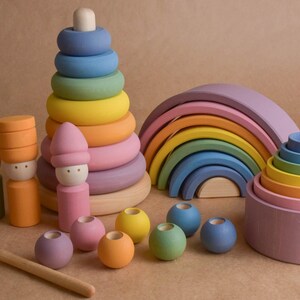 May include: A selection of brightly coloured wooden toys, including a rainbow arch, stacking rings, and peg dolls. The toys are in shades of blue, green, yellow, orange, and pink. The toys are designed for children.