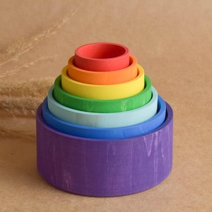 May include: A colourful wooden stacking toy, featuring seven nested rings in a rainbow of colours: red, orange, yellow, green, light blue, dark blue, and purple. This toy is designed for children's play and educational use.