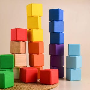 May include: A set of colorful wooden blocks stacked in different heights. The blocks are red, yellow, blue, green, purple, and light blue. The blocks are arranged in a pattern, with the tallest stack in the center.