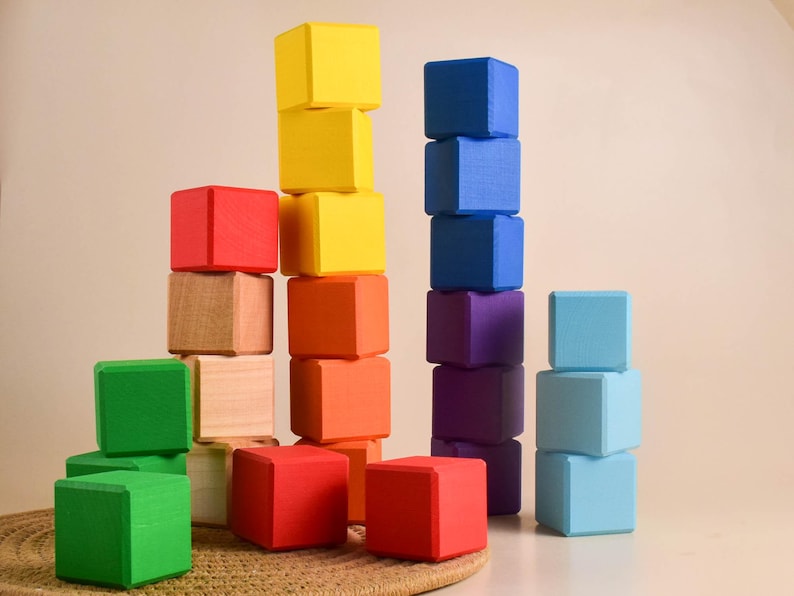 May include: A set of colorful wooden blocks stacked in different heights. The blocks are red, yellow, blue, green, purple, and light blue. The blocks are arranged in a pattern, with the tallest stack in the center.
