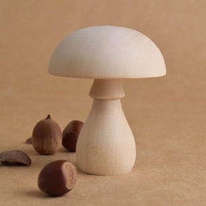 May include: A wooden mushroom-shaped decorative object with a rounded top and a bulbous base. Several brown acorns and acorn caps are scattered around the mushroom. The mushroom is made of light-colored wood.