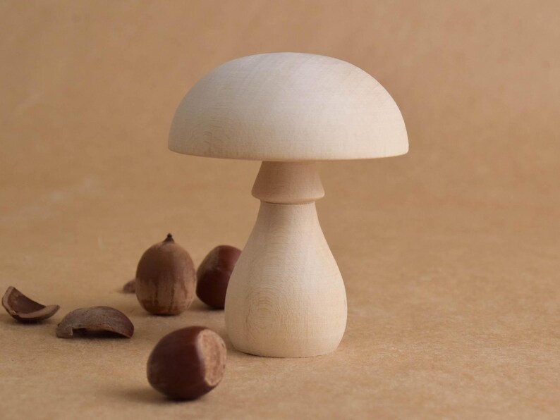 May include: A wooden mushroom-shaped decorative object with a rounded top and a bulbous base. Several brown acorns and acorn caps are scattered around the mushroom. The mushroom is made of light-colored wood.