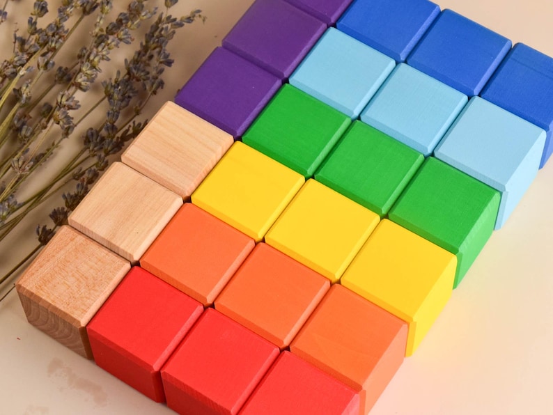 May include: A rainbow stack of wooden blocks, starting with natural wood and progressing through yellow, orange, red, green, blue, and purple.