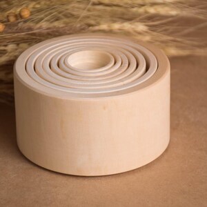 May include: A set of unfinished wooden nesting bowls, each fitting inside the next, creating a layered effect. The natural wood grain is visible, and the bowls are arranged on a neutral background. The largest bowl is approximately 5 inches in diameter.