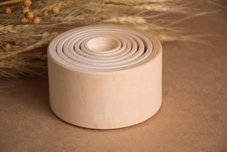 May include: A set of unfinished wooden nesting bowls, each fitting inside the next, creating a layered effect. The natural wood grain is visible, and the bowls are arranged on a neutral background. The largest bowl is approximately 5 inches in diameter.