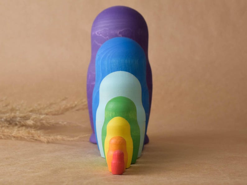 Pode incluir: Um conjunto de bonecas russas aninhadas com cores do arco-&iacute;ris. A maior boneca &eacute; roxa, seguida de azul, azul claro, verde, amarelo, laranja e vermelho.