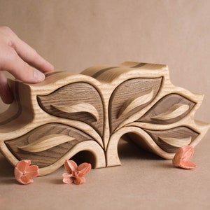 May include: A wooden jewelry box shaped like a tree with five leaf-shaped compartments. The box is made of light and dark wood and has a natural finish.