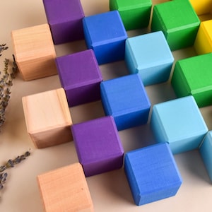 May include: A set of colorful wooden blocks arranged in a grid pattern. The blocks are painted in shades of blue, green, purple, yellow, and natural wood.