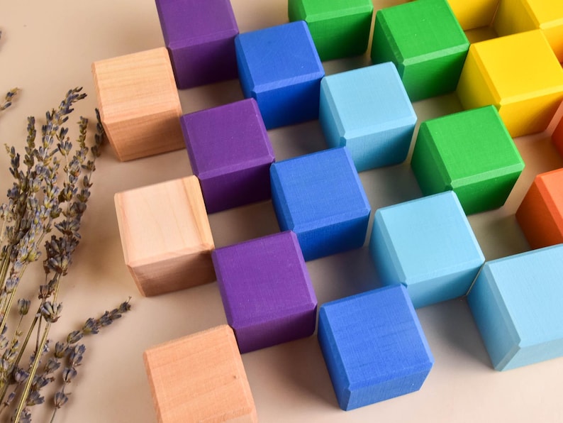 May include: A set of colorful wooden blocks arranged in a grid pattern. The blocks are painted in shades of blue, green, purple, yellow, and natural wood.