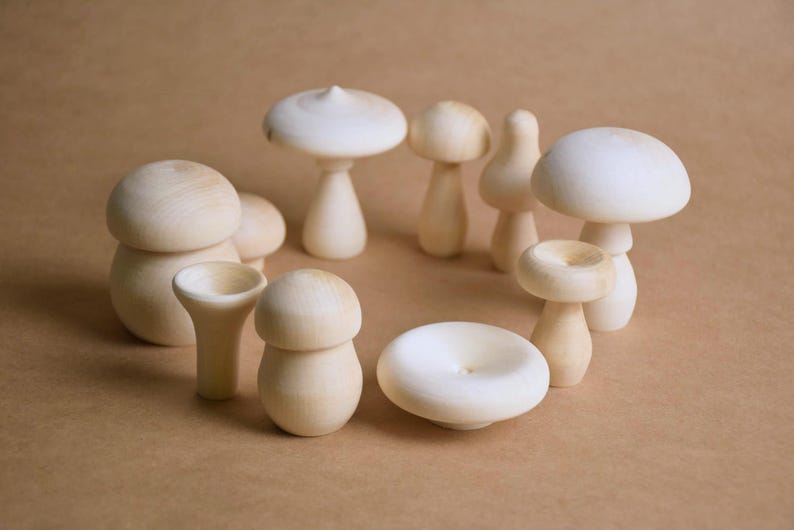 May include: A collection of wooden mushroom figurines in various shapes and sizes. The mushrooms are light-colored, with rounded caps and stems. They are arranged in a circular pattern against a neutral background.