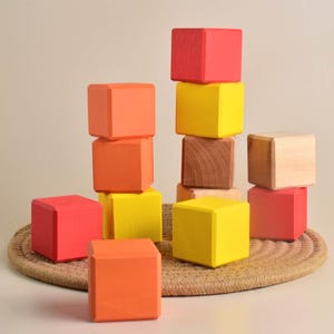 May include: A stack of colorful wooden blocks in red, orange, and yellow. The blocks are arranged in a pyramid shape, with the largest block at the bottom and the smallest block at the top.