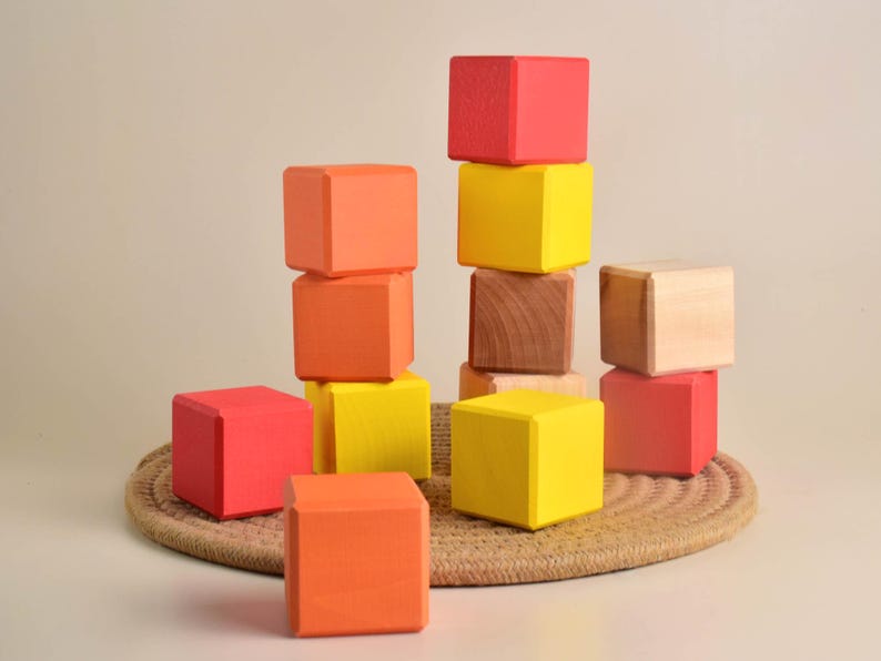 May include: A stack of colorful wooden blocks in red, orange, and yellow. The blocks are arranged in a pyramid shape, with the largest block at the bottom and the smallest block at the top.