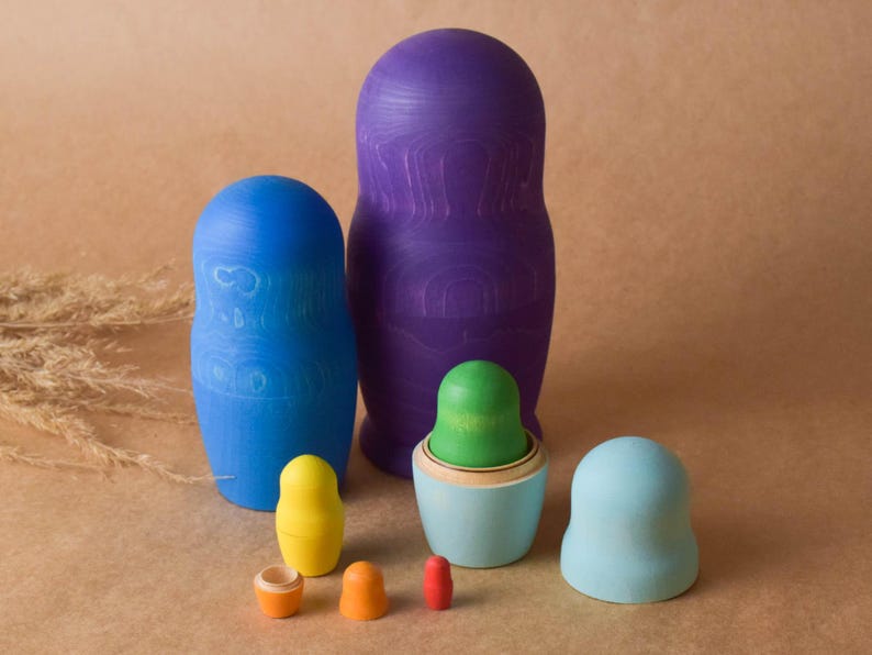 Pode incluir: Um conjunto de bonecas russas de madeira coloridas, ou bonecas de encaixe, de v&aacute;rios tamanhos. A boneca maior &eacute; roxa, a seguinte maior &eacute; azul e a menor &eacute; verde. Todas as bonecas s&atilde;o pintadas com desenhos simples.