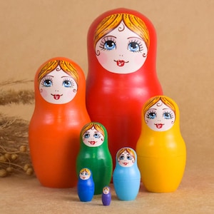 May include: A collection of six brightly coloured Matryoshka dolls, or Russian nesting dolls. The dolls are painted in shades of red, orange, green, yellow, and blue. Each doll has a painted face with blue eyes and a rosy complexion.