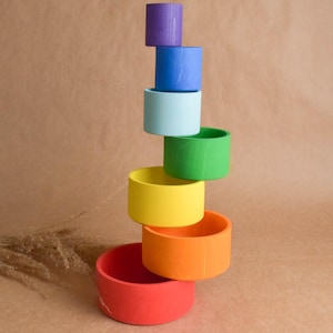 Peut inclure: Une pile de gobelets emboîtables en bois arc-en-ciel. Les gobelets sont peints dans différentes couleurs, en commençant par le violet en haut et en terminant par le rouge en bas. Les gobelets sont disposés en une tour, avec le plus grand gobelet en bas et le plus petit gobelet en haut.