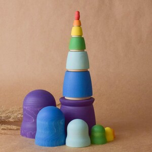 Pode incluir: Um brinquedo de empilhar de madeira com cores do arco-&iacute;ris com uma base azul, roxa e azul claro. O brinquedo &eacute; feito de madeira natural e &eacute; pintado em cores brilhantes.