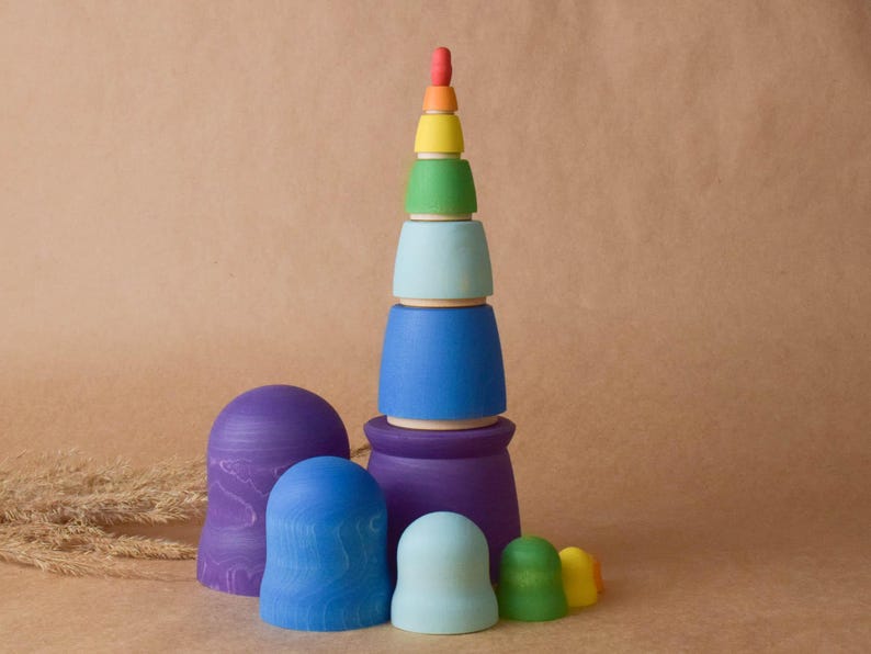 Pode incluir: Um brinquedo de empilhar de madeira com cores do arco-&iacute;ris com uma base azul, roxa e azul claro. O brinquedo &eacute; feito de madeira natural e &eacute; pintado em cores brilhantes.