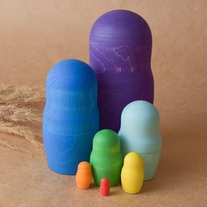 Pode incluir: Um conjunto de seis bonecas russas de encaixe, tamb&eacute;m conhecidas como bonecas matryoshka. As bonecas s&atilde;o pintadas em um arco-&iacute;ris de cores, come&ccedil;ando com roxo, azul, azul claro, verde, amarelo e laranja. A menor boneca &eacute; vermelha.