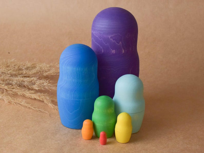 Pode incluir: Um conjunto de seis bonecas russas de encaixe, tamb&eacute;m conhecidas como bonecas matryoshka. As bonecas s&atilde;o pintadas em um arco-&iacute;ris de cores, come&ccedil;ando com roxo, azul, azul claro, verde, amarelo e laranja. A menor boneca &eacute; vermelha.