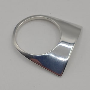 May include: A polished silver ring featuring a smooth, circular band that transitions into a wide, flat, triangular-shaped face. The metal surface is reflective and solid, showcasing a clean, geometric design with sharp, defined edges and a high-shine finish.