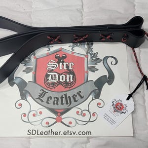 May include: Black leather riding crop with red cross-stitching and a red and black cord. The crop is lying on a white surface with a logo that says "Sire Don Leather" and the website SDLeather.etsy.com.