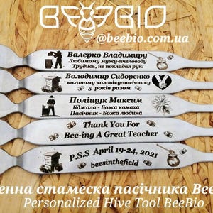 May include: Five personalized hive tools with engraved messages. The tools are made of metal and have a curved handle. The messages include names, dates, and sentiments like "Thank You For Bee-ing A Great Teacher".