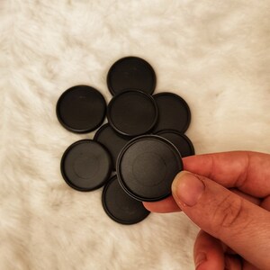 May include: A group of eight black round plastic discs, one of which is being held by a hand.