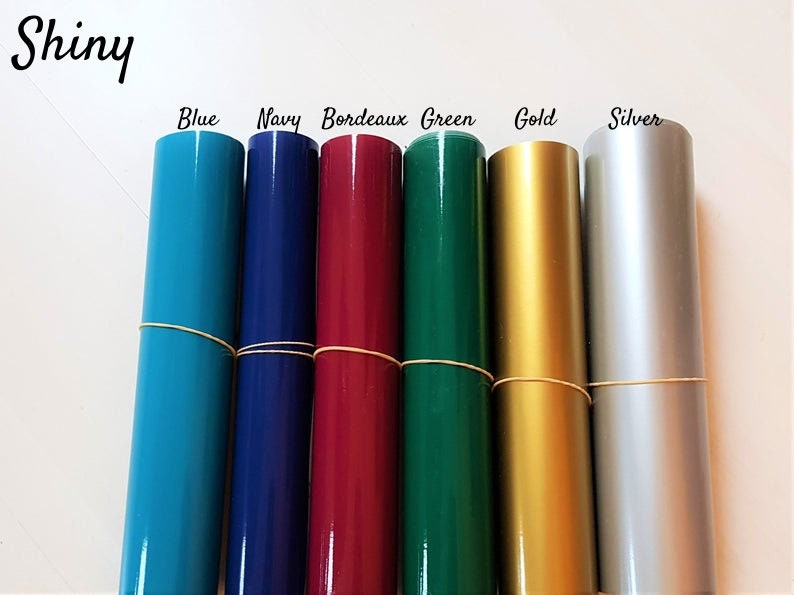 May include: Seven rolls of shiny vinyl in various colors: blue, navy, burgundy, green, gold, and silver. The rolls are wrapped with rubber bands.