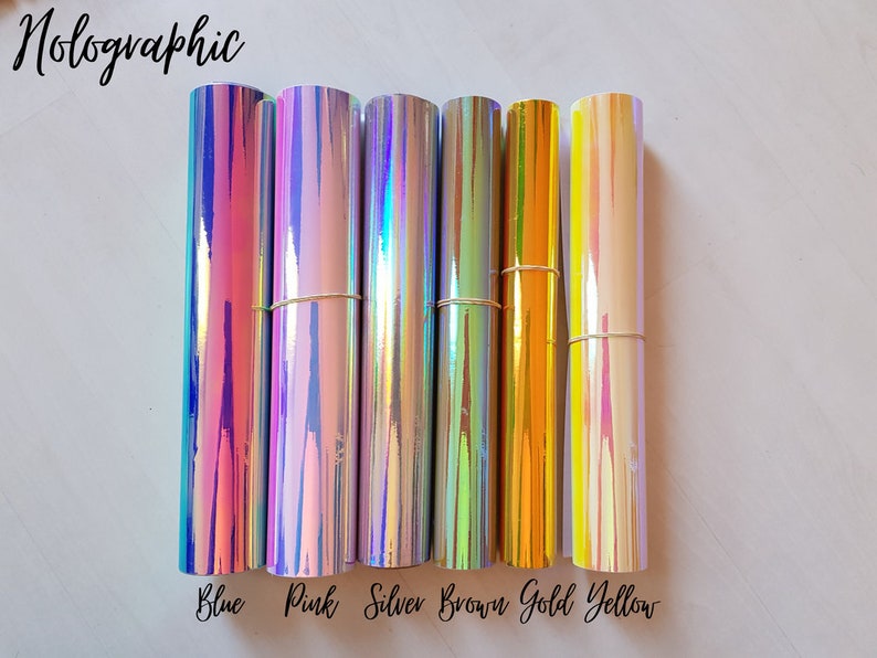 May include: Seven rolls of holographic vinyl in various colors, including blue, pink, silver, brown, gold, and yellow. The rolls are arranged horizontally, with the colors labeled below each roll.
